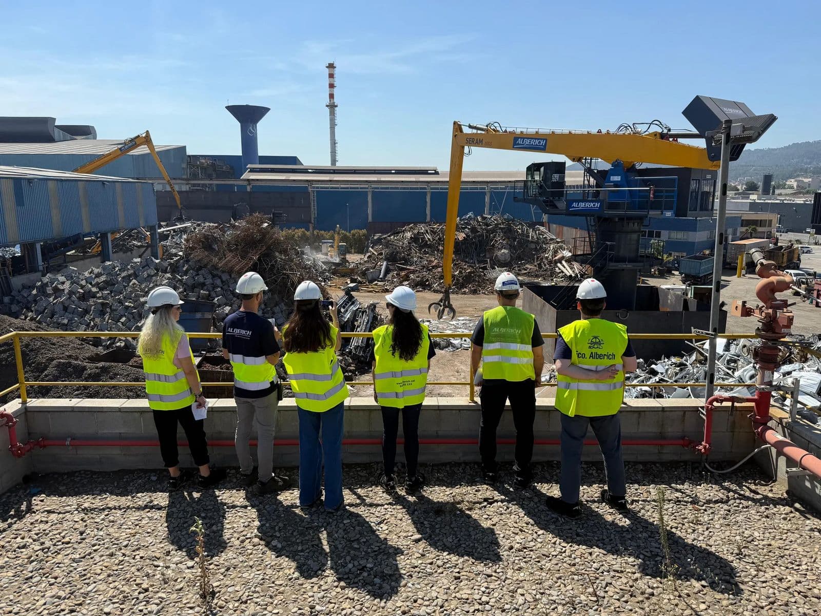 Equipo de Alberich con casco y chaleco observando el patio de chatarra desde una terraza