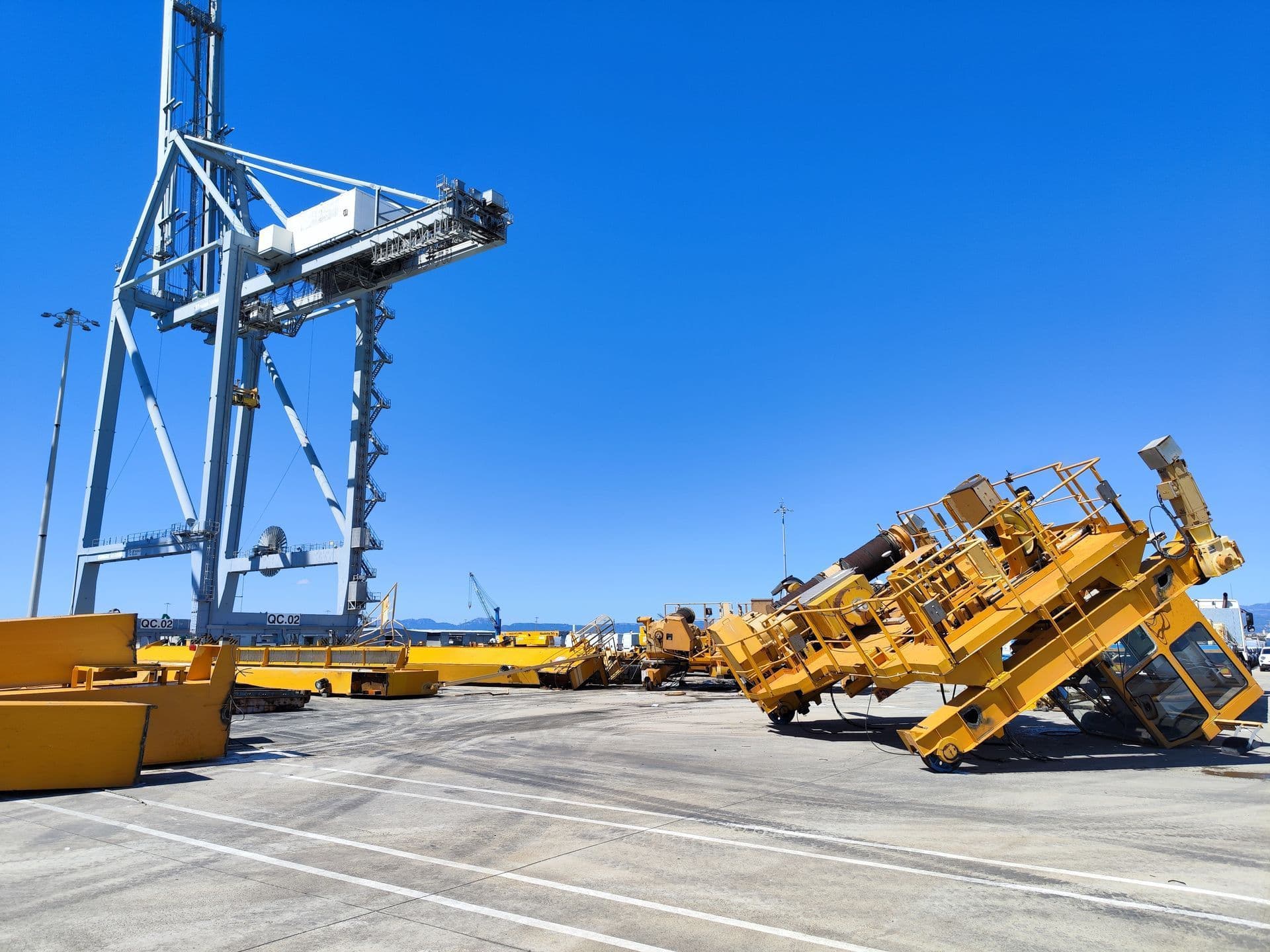 Peces d’una grua portuària RTG desmuntada al moll, al costat d’una grua de contenidors