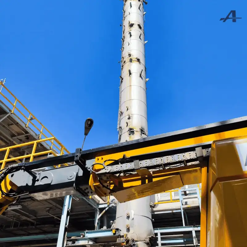 30-metre distillation column seen from its base, with the yellow arm of a machine in the foreground