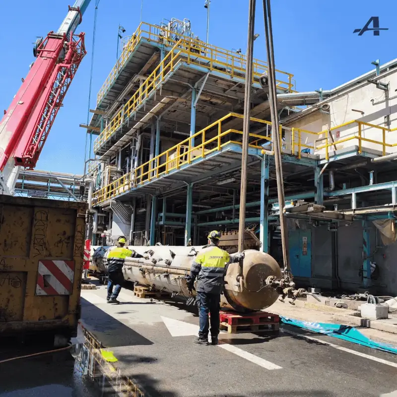 Two operatives guide a section of the distillation column resting on the ground and held by the crane slings